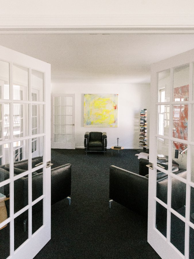 A therapy room seen through open french doors, with a leather chair beneath an abstract painting
