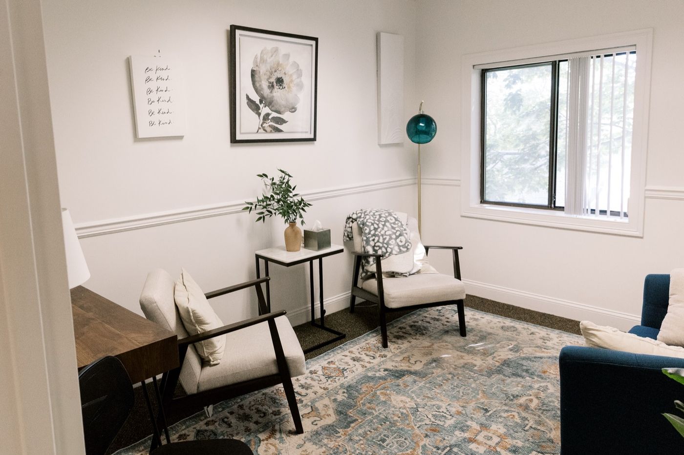 A calm, kind therapy room at CMHS in Milford with soft chairs, a plant, and a framed ‘Be Kind’ print